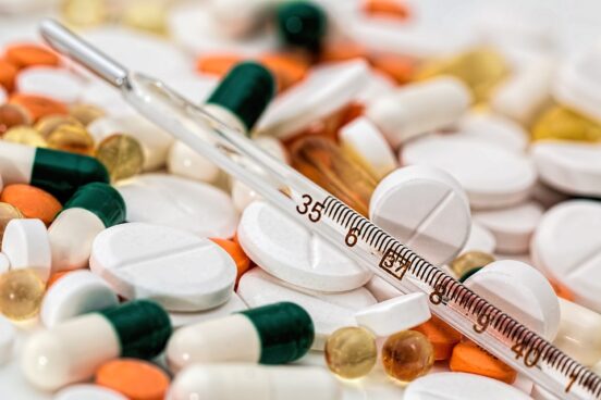 Bild, allehanda läkemedel (tabletter, kapslar) i olika färger, samt en termometer